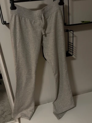 Grå mjukisbyxor från Nelly - Superbekväma grå mjukisbyxor från Nelly med bred resår i midjan och dragsko. Byxorna har raka ben och är tillverkade i ett mjukt och stretchigt material som känns skönt mot huden. Perfekta för chill dagar hemma eller när du vill vara extra comfy.