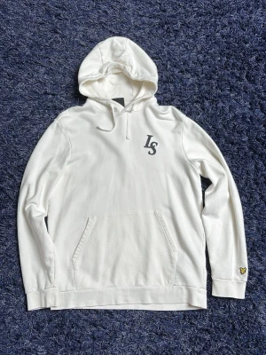 Vit hoodie från Lyle & Scott - Snygg vit hoodie från Lyle & Scott med LS-logga på bröstet och den klassiska gula örnpatchen på ärmen. Hoodien har känguruficka framtill, dragsko i huvan och ribbade muddar. Perfekt för en clean och stilren look. Kolla sista bild där en fläck syns på tröjan, hör av er vid minsta fundering!
