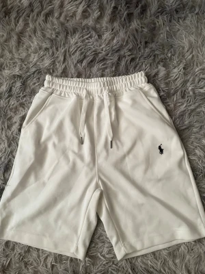 Vita shorts från Polo Ralph Lauren -  Du kan köpa shortsen och T-shirten för 500. Kolla min profil.  Snygga vita shorts från Polo Ralph Lauren med klassisk broderad logga på vänster ben. Shortsen har elastisk midja med snörning och två sidofickor. Perfekta för sommaren och tillverkade i mjuk bomull för maximal komfort.