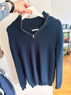 Mörkblå stickad tröja från Zara - Mörkblå stickad tröja från Zara med hög krage och dragkedja framtill. Tröjan har lång ärm och ribbstickad struktur som ger en clean och stilren look. Perfekt för lager på lager och funkar till det mesta.