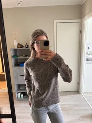 Gråbrun stickad tröja - Mysig gråbrun stickad tröja med rund halsringning och långa ärmar. Tröjan har en enkel, klassisk design med ribbstickade muddar vid ärmslut och nederkant. Perfekt för lager på lager och passar till det mesta i garderoben.
