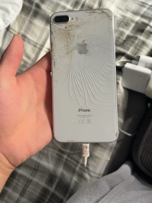  iPhone 8 Plus  - Säljer en vit iPhone med dubbla bakre kameror och klassisk rund hemknapp. Baksidan är i glas med Apple-loggan i silver och telefonen har en elegant, avlång form. Perfekt för dig som gillar stilren design och vill ha en pålitlig smartphone.
