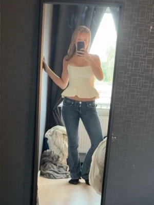 Vit peplum linnetopp med tunna band - Säljer en vit linnetopp med tunna axelband och peplumvolang nedtill. Toppen har en figurnära passform upptill och är lätt utsvängd vid midjan för en snygg siluett. Perfekt att styla med jeans eller kjol för en trendig look.