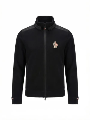 Svart fleecejacka från Moncler - Stilren svart fleecejacka från Moncler med dragkedja framtill och broderad logga på bröstet. Jackan har hög krage, quiltade axelpartier och diskreta röda och vita detaljer vid krage och ärmslut. Perfekt för kyliga dagar.