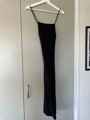 Svart klänning med tunna axelband - En stilren svart klänning med tunna axelband och rak passform. Klänningen har minimalistisk design och är perfekt för dig som gillar en enkel men elegant look. Materialet känns mjukt och följsamt mot kroppen.