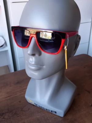 Röda solglasögon från Sunshine  - Coola solglasögon från Sunshine med röd båge och mörka glas. Klassisk form som passar till många stilar. Perfekta för soliga dagar och ger en snygg touch till din outfit.