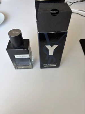 Yves Saint Laurent Y Eau de Parfum - Yves Saint Laurent Y Eau de Parfum med stilren, fyrkantig glasflaska i svart och transparent design. Flaskan har en metallisk etikett och ett matchande svart lock. Kommer med originalkartong i svart med blå detaljer.