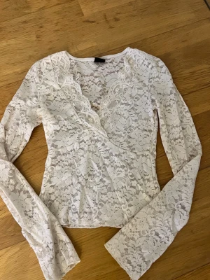 Vit spetsblus med omlott och v-ringning - Snygg vit blus i spets med omlott och v-ringning. Långärmad modell med fina spetsdetaljer och figurnära passform. Perfekt för dig som gillar romantisk och trendig stil.