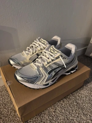 Asics Gel-Kayano 14  - Säljer ett par Asics Gel-skatans 14 sneakers i white/graphite grey storlek 42. Skorna har meshpaneler och ventilation, snygga reflekterande partier och klassisk snörning. Platt sula och rund tå ger en sportigt vibe, perfekt för dig som gillar retrostil och komfort.   De är helt nya och oanvända, säljer de då den storleken inte passade mig.  OBS! Skorna kommer utan skokartong.