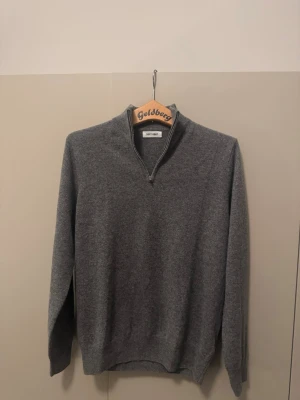 Grå halvzip-tröja från Soft Goat - Mysig grå tröja från Soft Goat i kashmir med halv dragkedja vid kragen. Klassisk och stilren modell med lång ärm och ribbade muddar. Perfekt för lager-på-lager och passar till det mesta.