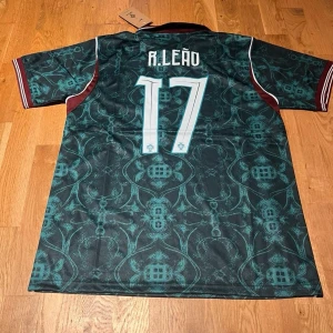 Portugal green R.Leao #17 - Snygg Portugal matchtröja från Nike med R. Leão och nummer 17 på ryggen. Tröjan är mörkgrön med mönster, vinröda detaljer och vita ränder på ärmarna. Klassisk krage och korta ärmar. Perfekt för dig som älskar fotboll och vill sticka ut på planen.