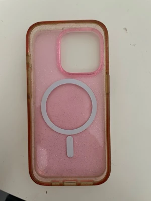 Rosa MagSafe mobilskal med glitter - Snyggt rosa mobilskal med glittereffekt och MagSafe-kompatibilitet. Skalets kanter är transparenta med en lätt brun ton och baksidan har en tydlig MagSafe-ring i vitt. Passar perfekt för dig som vill ha ett skal som sticker ut och funkar med MagSafe-laddare.