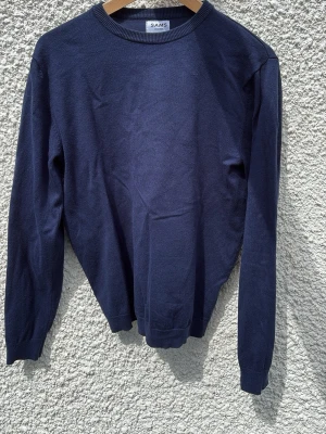 Mörkblå tröja från SAMS - En stilren mörkblå tröja från SAMS med rund halsringning och långa ärmar. Tröjan har ribbade muddar vid ärmslut och nederkant. Perfekt att matcha med jeans eller chinos för en clean look.