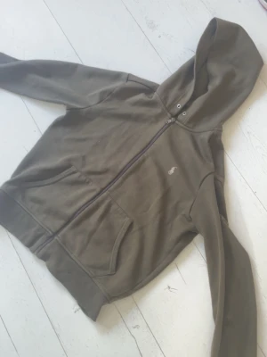 Olivgrön hoodie från Polo Ralph Lauren - Snygg olivgrön hoodie med dragkedja från Polo Ralph Lauren. Klassisk design med huva, två fickor framtill och den ikoniska lilla loggan broderad på bröstet. Perfekt för en avslappnad och stilren look.