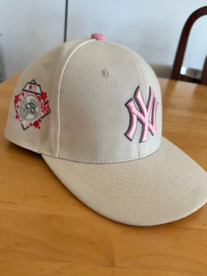  New Era NY Keps med Rosa detaljer - Snygg beige keps från New Era med New York Yankees-logga i rosa brodyr framtill. 
