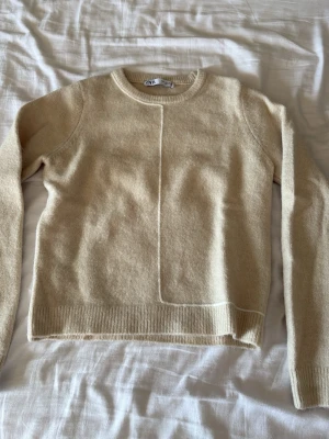 Beige stickad tröja från ZARA - Säljer en beige stickad tröja från ZARA med rund halsringning och långa ärmar. Tröjan har en unik sömdetalj framtill och baktill samt ribbade muddar vid ärmslut och nederkant. Perfekt för dig som gillar minimalistisk och stilren design.