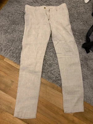 linnebyxor från NN07 - Snygga beiga linnebyxor från NN07 med rak passform och klassisk design. Byxorna har dragkedjegylf och knapp i midjan. Perfekta för en avslappnad och stilren look under varmare dagar.