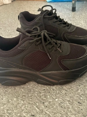 Chunky svarta sneakers med meshdetaljer - Säljer ett par chunky svarta sneakers med coola meshdetaljer och kraftig sula. Skorna har snörning och en sportig vibe, perfekta för dig som gillar streetstyle. Materialet är en mix av syntet och mesh för extra komfort och andningsförmåga.