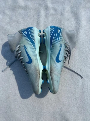 Nike Mercurial fotbollsskor - Säljer ett par fotbollsskor från Nike med blå detaljer och högt skaft. Skorna har snörning och high sock som är tillverkade för bättre bollkontroll. Perfekta för dig som vill sticka ut på planen. Är i storlek 40,5.