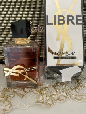 Yves Saint Laurent Libre Le Parfum - Yves Saint Laurent Libre Le Parfum med elegant glasflaska, svart fyrkantigt lock och guldiga detaljer. Doften kommer i en lyxig förpackning med YSL-logga i guld. Perfekt för dig som gillar exklusiva och trendiga parfymer.