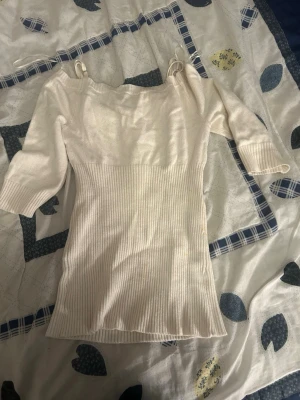 Vit ribbad topp från Guess - Snygg vit ribbad topp från Guess med trekvartsärm och smala axelband. Toppen har en figurnära passform och är tillverkad i ett mjukt stickat material som ger en bekväm känsla. Perfekt för dig som gillar stilrena och trendiga plagg.