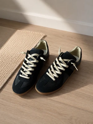 Svarta sneakers med vita snören från maison margiela  - Stilrena svarta sneakers med kontrasterande vita snören och beige innersula. Skorna har en klassisk låg siluett och gummisula. Materialet är en mix av mocka och läder för en snygg och tidlös look. Kvitto finns och box.
