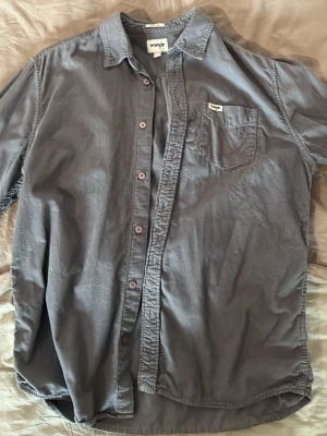 Ljusblå skjorta från Wrangler - Snygg ljusblå skjorta från Wrangler med klassisk krage och bröstficka med logotyp. Skjortan har knappar framtill och är tillverkad i mjuk bomull. Perfekt för en avslappnad och stilren look.