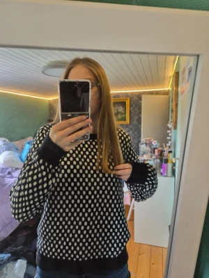 Svartvit stickad tröja Michael Kors - Snygg stickad tröja från Michael Kors i svart med vita prickar. Tröjan har rund halsringning, långa ärmar och ribbade muddar vid ärmslut och nederkant. Perfekt för dig som gillar trendiga och bekväma plagg med coolt mönster.