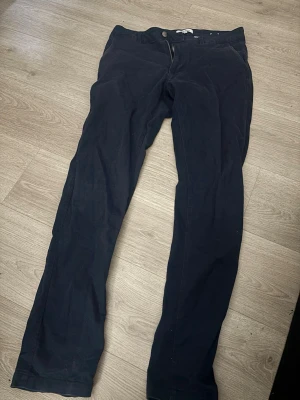 Mörkblå chinos med rak passform - Snygga mörkblå chinos med rak passform och klassisk design. Byxorna har framfickor, bakficka med knapp och stängs med dragkedja och knapp. Perfekta för en stilren look. 