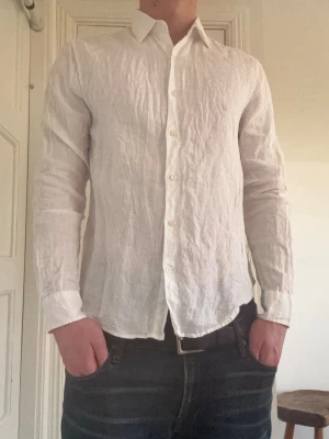 Vit linneskjorta - Klassisk vit skjorta i linne med lång ärm och knäppning framtill. Skjortan har en avslappnad passform och krage, perfekt för en stilren och luftig look. Passar dig som gillar enkel och tidlös stil.