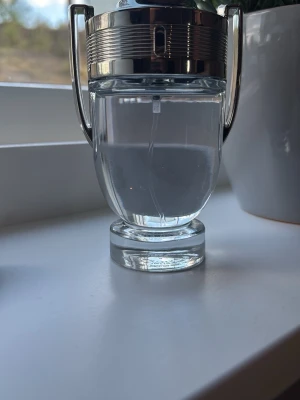 Paco Rabanne Invictus parfym - Säljer en Paco Rabanne Invictus parfym i en unik troféformad flaska med silverfärgade detaljer. Flaskan är genomskinlig och visar den klara vätskan inuti. Perfekt för dig som gillar stilrena och moderna dofter.