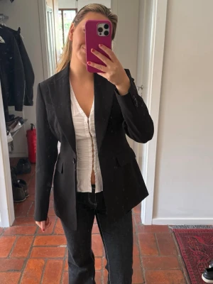 Svart kavaj med figursydd passform - Stilren svart kavaj med klassisk krage och knäppning framtill. Kavajen har två fickor med lock och är långärmad. Passar perfekt till både jeans och kostymbyxor. Snygg och tidlös modell som ger en dressad look. Från Hm men köpt via Sellpy 