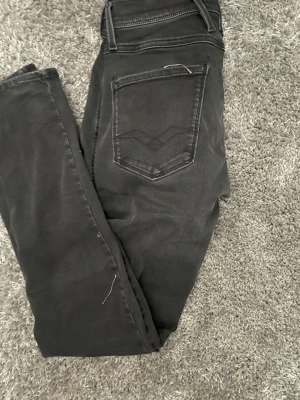 Svarta Replay jeans med smal passform - Snygga svarta jeans från Replay med smal passform och klassisk femficksdesign. Jeansen har diskreta slitningar och Replay-logga på fickan fram. Tillverkade i mjukt denimtyg som ger en bekväm känsla och stilren look.