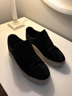 Mocka skor från Selected homme - Stilrena svarta sneakers med ovandel i mocka-liknande material och vita sulor. Klassisk låg modell med svarta skosnören och diskret design som passar till det mesta. Perfekta för dig som gillar en clean och enkel stil.