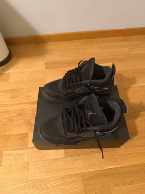 Svarta Air Jordan 4 Retro sneakers - Säljer ett par helsvarta Air Jordan 4 Retro sneakers med klassisk siluett. Skorna har ovandel i mocka och mesh, samt detaljer i plast och gummi. Ikonisk Jumpman-logga på plösen och hälen. Perfekta för dig som gillar streetwear och sportig stil.