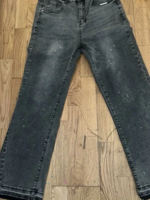 Flared jeans - Säljer ett par grå jeans med tvättad look och raka ben. Jeansen har klassisk femficksmodell och knappgylf. Materialet är denim med en lätt sliten finish och små vita detaljer för en trendig vibe.
