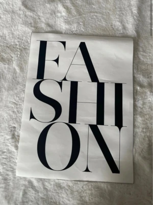 Poster med texten FASHION - Snygg poster med ordet FASHION i stora svarta bokstäver på vit bakgrund. Perfekt som dekoration för dig som gillar mode och stilrena detaljer. Tryckt på papper med modern och minimalistisk design.