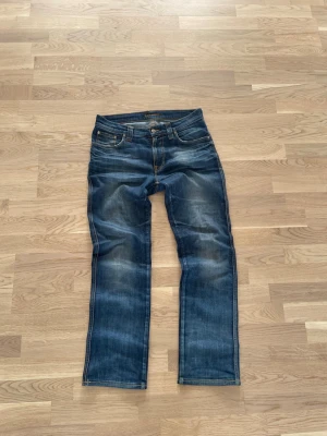 Blå jeans från Nudie Jeans i modellen Slim Jim - Säljer ett par klassiska blå jeans från Nudie Jeans i modellen Slim Jimmed snygga slitningar och kontrastsömmar. Modellen har fem fickor, normal midja och raka ben. Perfekta för en avslappnad och trendig stil. Går ner i pris vid snabb affär!