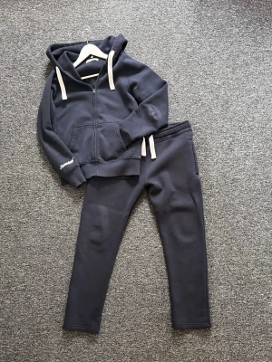 Russemerch set (M) - Säljer ett mörkblått mjukisset från Russemerch med dragkedja, huva och vita snören. Setet består av en hoodie med fickor och matchande byxor med dragkedja vid fickorna.                  -Nypris: 1250kr.                                                                              -Skick: 9/10.                                                       Hör gärna av dig vid frågor och funderingar!