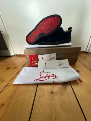 Christian Louboutin svarta sneakers - Snygga svarta sneakers från Christian Louboutin med den ikoniska röda sulan. Skorna är låga och har en stilren design i mocka. Kommer med originalkartong, dustbag och äkthetskort. Perfekta för dig som vill sticka ut med exklusiva detaljer. Sulan är smutsig pga att jag inte har tvättat dom. Om ni vill ha fler bilder hör av er! Skorna funkar också till folk som har 40-42