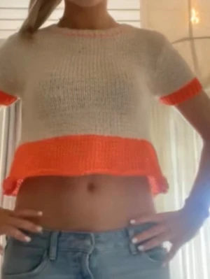 Stickad kortärmad topp med orange detaljer - Trendig stickad topp i vitt med korta ärmar och kontrasterande orange ribbade kanter vid ärmslut, nederkant och halsringning. Modellen är croppad och har en avslappnad passform, perfekt till jeans eller kjol. Materialet är mjukt och lättstickat.