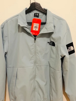 Ljusblå vindjacka från The North Face - Ljusblå vindjacka från The North Face sprillans ny. Jackan ar logga på bröstet och ärmen och även på ryggen , samt lätt material som skyddar mot vind och regn.