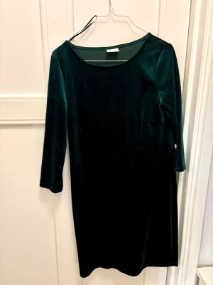 Mörkgrön sammetsklänning - Mörkgrön klänning i mjuk sammet med rund halsringning och trekvartsärm i en tajt passform. Enkel och stilren design med rak passform som ger en klassisk look. Perfekt till både kontoret men också lite mer högtidliga tillställningar ✨ Jättefint skick, endast använd fåtal gånger 🤩
