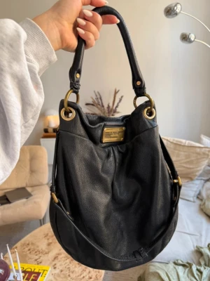 Svart Marc by Marc Jacobs handväska - Snygg svart handväska i mjukt läder från Marc by Marc Jacobs. Väskan har guldfärgade metalldetaljer, dubbla handtag och en metallbricka framtill med logga. 
