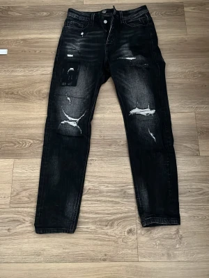 Svarta ripped jeans från Alessandro - Snygga svarta jeans från Alessandro med slitna detaljer och hål på benen. Jeansen har en smal passform och klassisk femficksdesign. Perfekta för dig som gillar en edgy och trendig stil.
