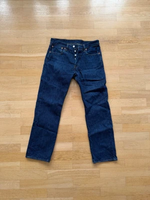 Levi's blå raka jeans 31/30 storlek - Säljer ett par klassiska blå Levi's jeans med rak passform och knappgylf. Jeansen har fem fickor, kontrastsömmar och den ikoniska läderlappen bak i midjan. Perfekta för en avslappnad och tidlös stil.
