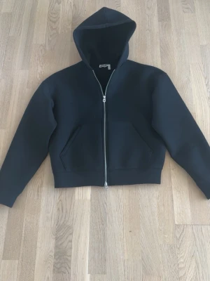 Svart hoodie med dragkedja från weekday - Säljer en svart hoodie från weekday med dragkedja framtill och två stora fickor. Tillverkad i ett tjockare material som känns riktigt lyxigt och stilrent. Passar i xs också.