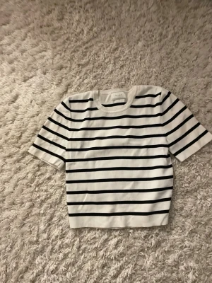 Randig vit och svart topp från Zara Knit - Kortärmad topp från Zara Knit i vitt med svarta horisontella ränder. Klassisk rund halsringning och rak passform. Perfekt till jeans eller kjol för en enkel och stilren look.