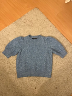 Blå stickad tröja med puffärm - Mysig blå stickad tröja med puffärmar och rund hals. Tröjan har ribbade muddar vid ärmslut och nederkant, samt en något kortare och boxig passform. Perfekt för dig som gillar en trendig och avslappnad stil. 
