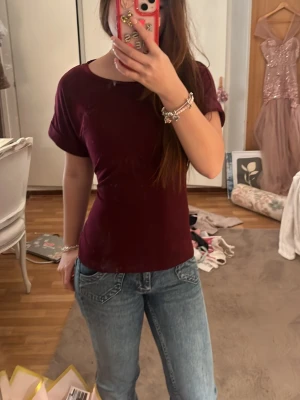 Vinröd topp med knyt i ryggen - Snygg vinröd topp med korta ärmar och rund halsringning. Toppen har ett dekorativt knyt i ryggen som ger en unik touch. Passformen är normal och materialet känns mjukt och bekvämt, perfekt till jeans eller kjol.